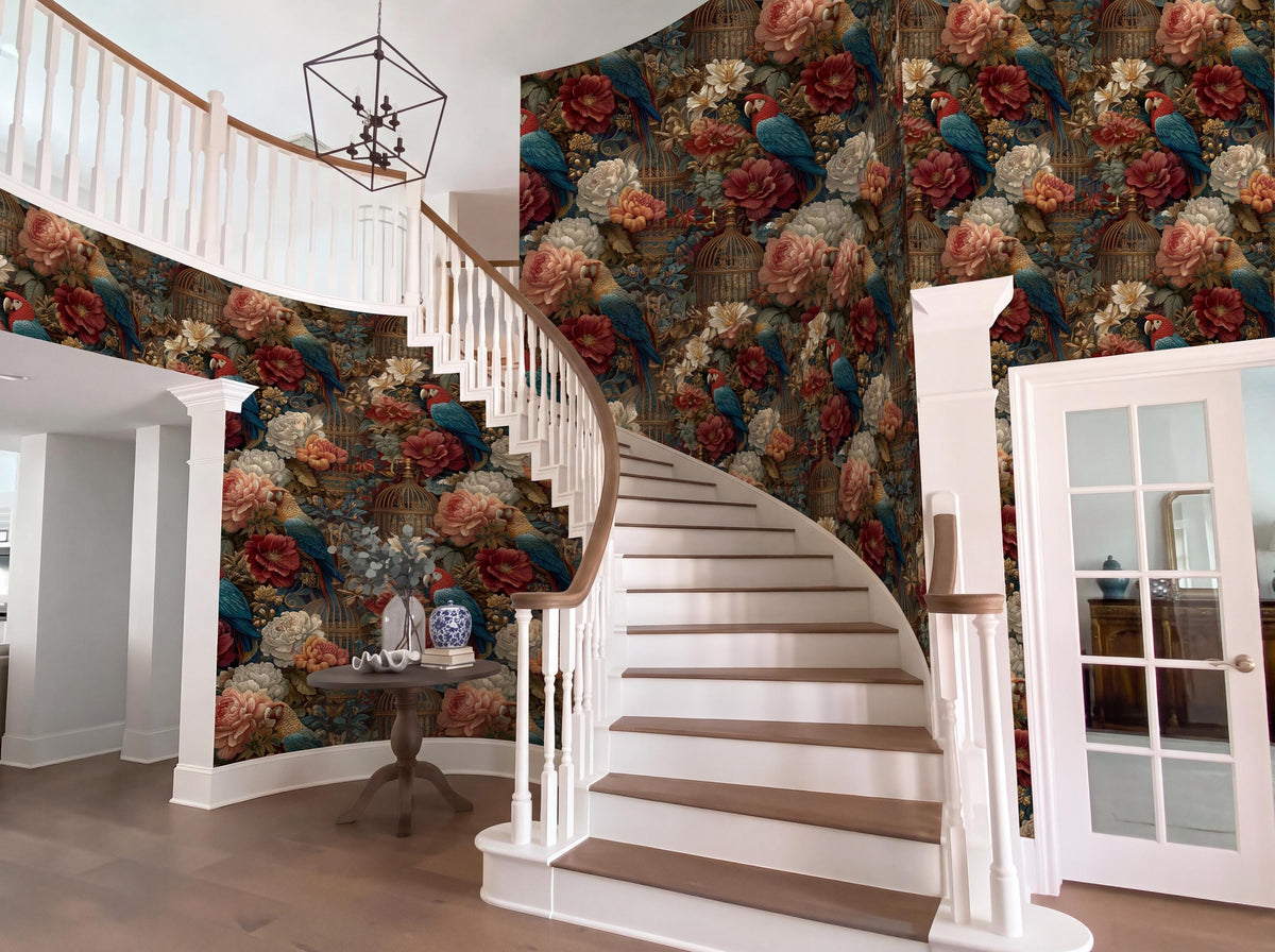 a grand staircase with a floral wallpaper, a white railing, and a chandelier hanging from the ceiling. The staircase is set against a wall with a vibrant floral pattern. The room also features a table with a vase and a potted plant, and a door with a glass window.