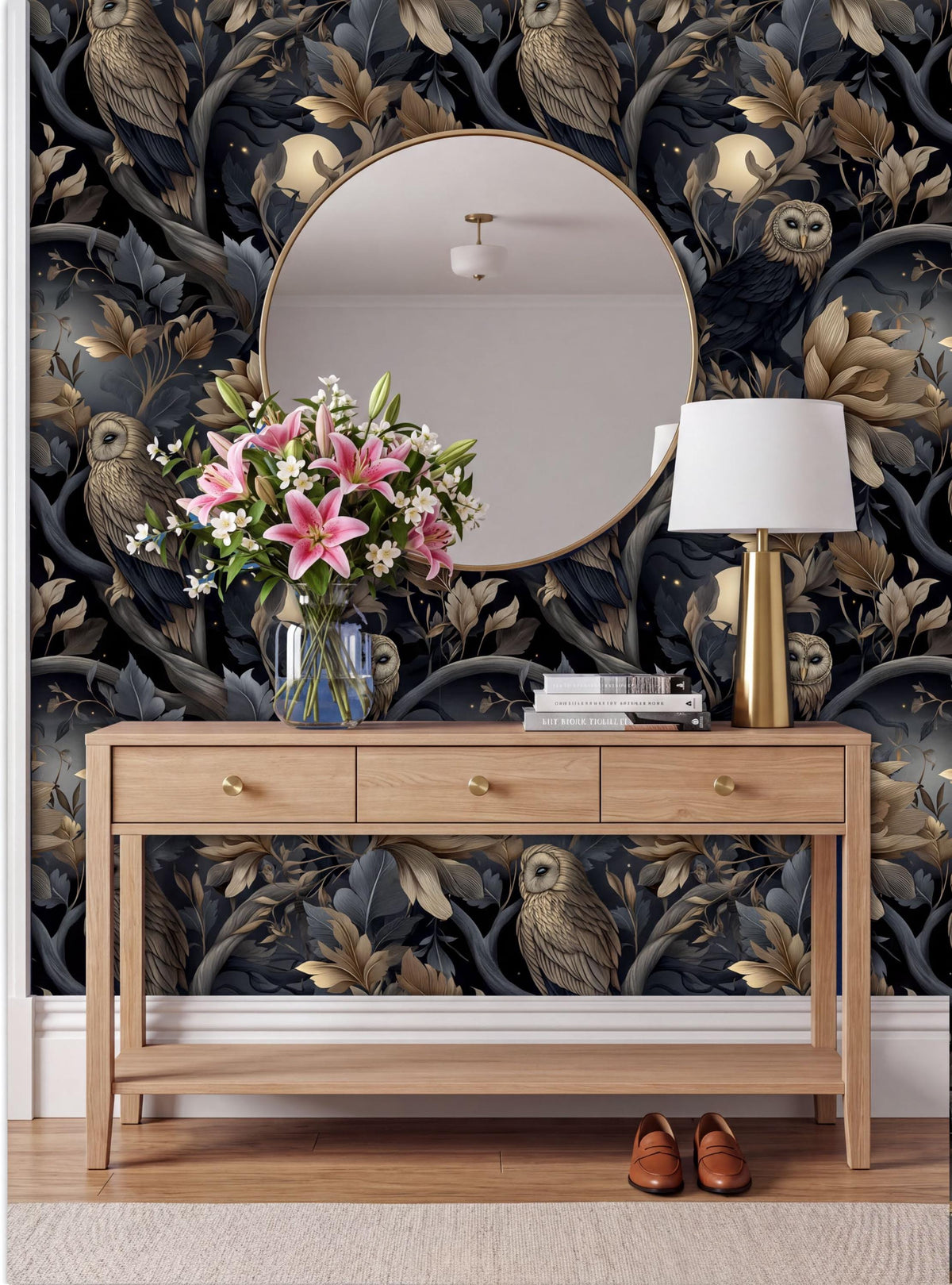 a wooden console table with a round mirror above it, a vase of pink flowers, a lamp, and a pair of brown shoes placed on the floor. The wall behind the table has a dark, ornate wallpaper with a pattern of owls and flowers.