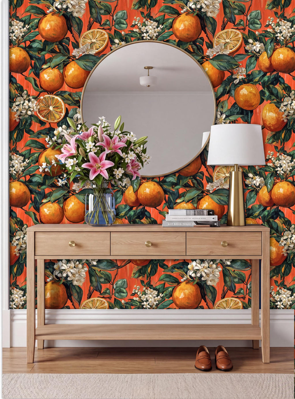 a wooden console table with a round mirror above it, set against a vibrant orange wall with a floral pattern. The table has a vase of flowers and a lamp on it, creating a cozy and inviting atmosphere.