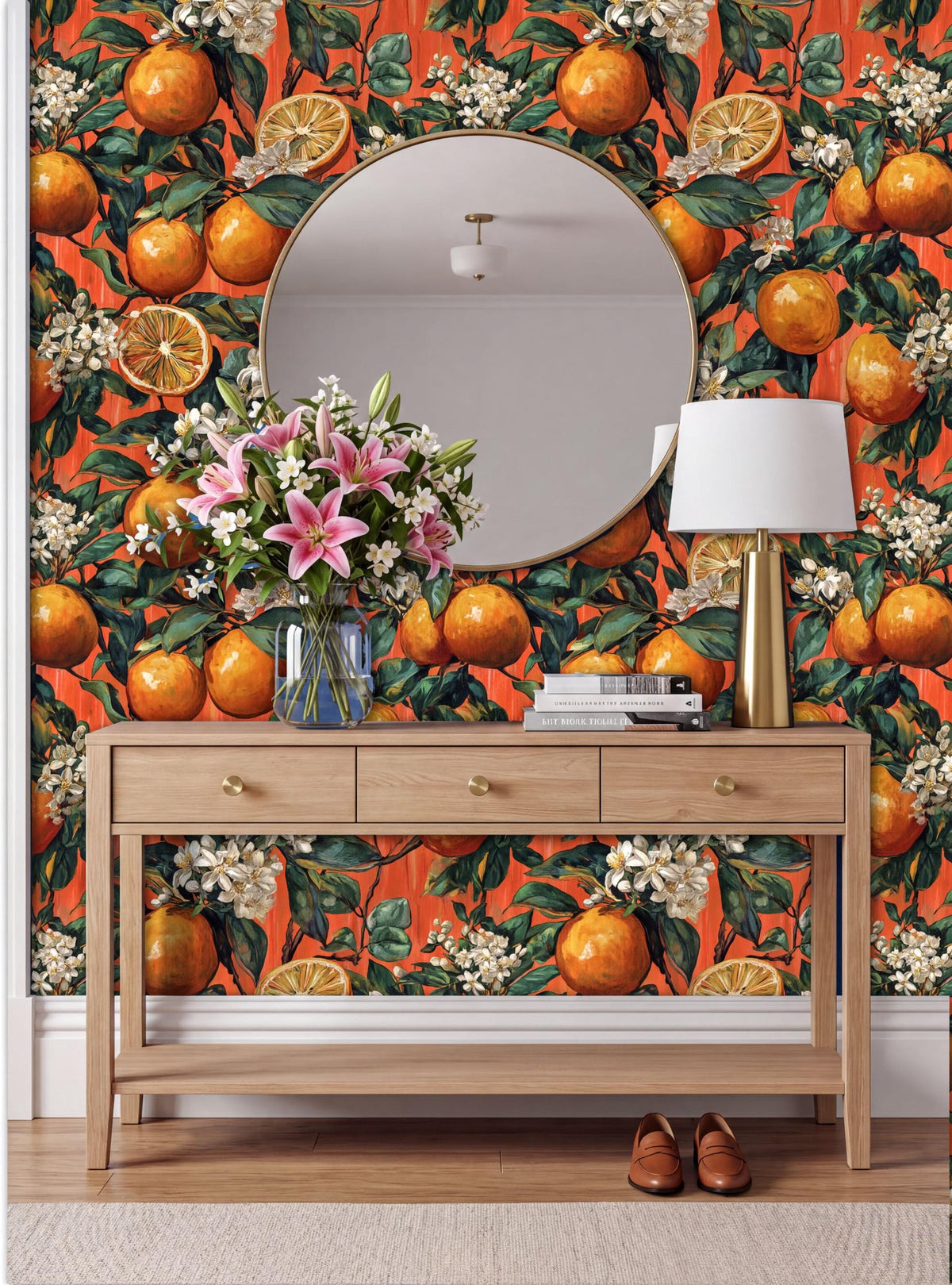 a wooden console table with a round mirror above it, set against a vibrant orange wall with a floral pattern. The table has a vase of flowers and a lamp on it, creating a cozy and inviting atmosphere.