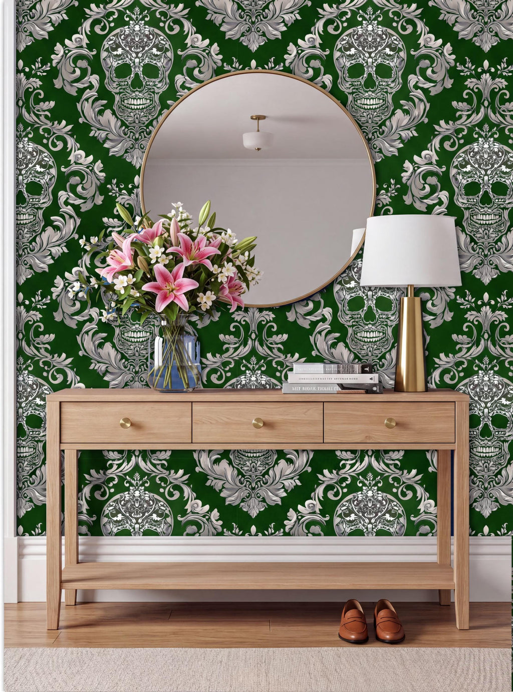 a wooden console table with a round mirror above it, set against a wall with a green and white damask pattern. The table has a vase of pink flowers and a lamp on it.