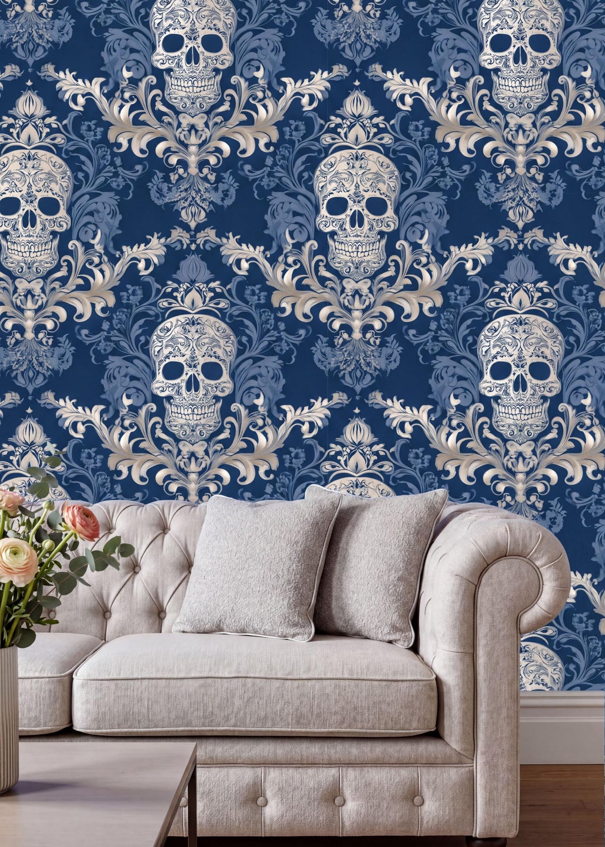 a living room with a white tufted sofa and a vase of flowers on a coffee table. The sofa is positioned against a wall with a repeating pattern of blue and white damask wallpaper, which includes a repeating pattern of skull designs.