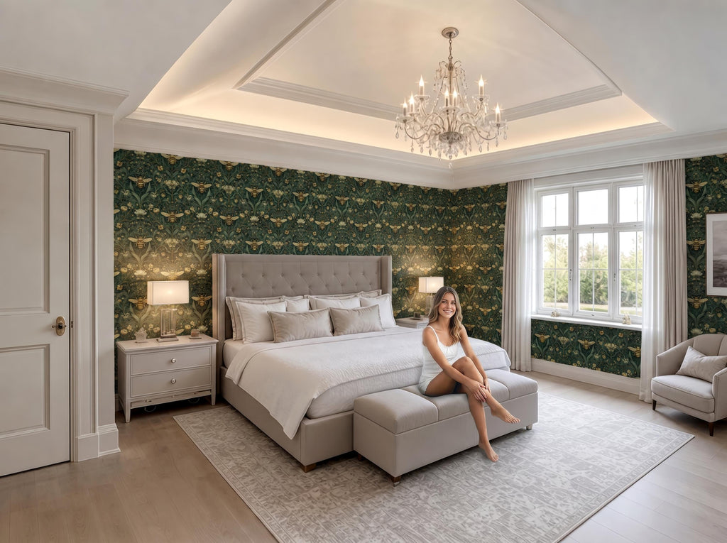 A woman sits on a bench in a luxurious bedroom with a large bed, a chandelier, and a patterned wallpaper.