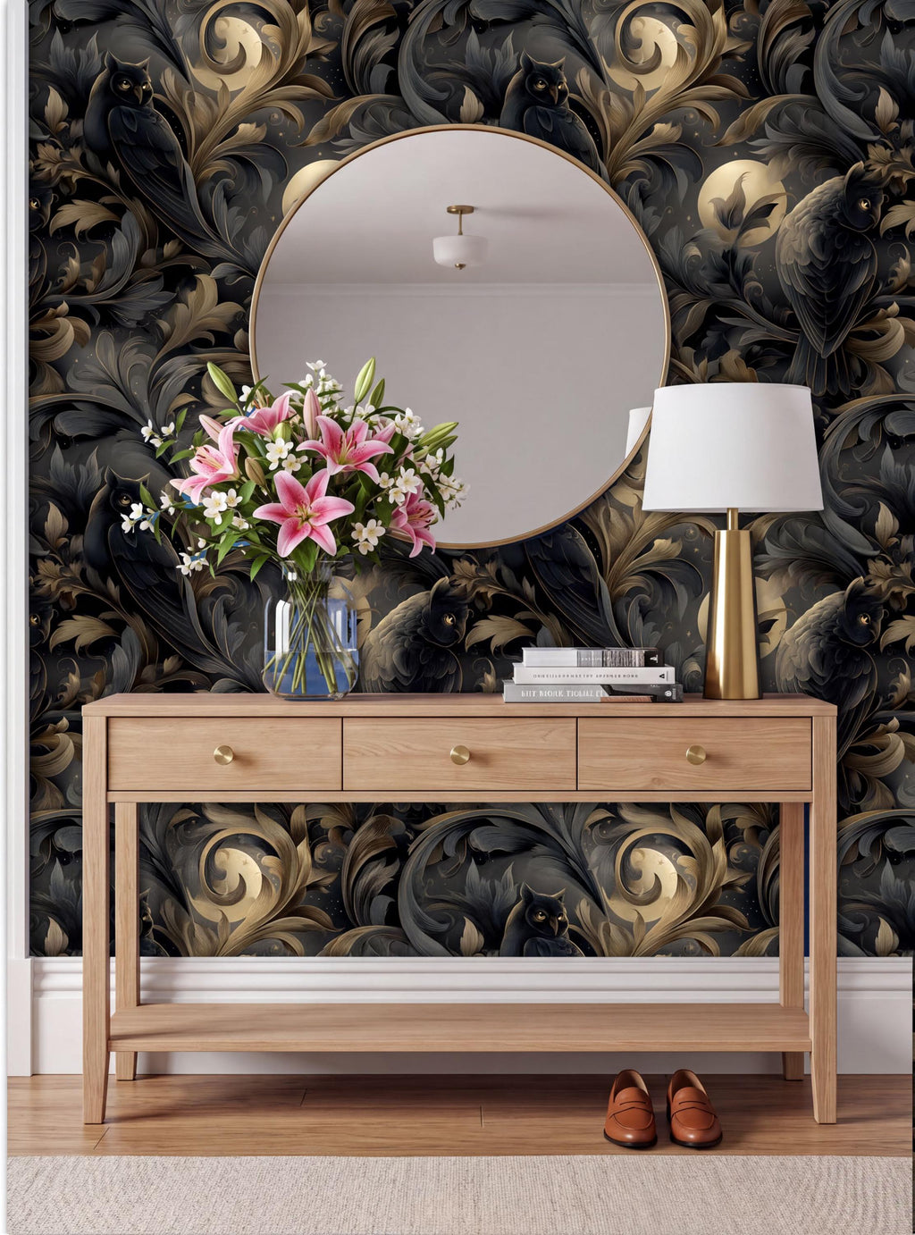 a wooden console table with a vase of pink flowers, a round mirror, a lamp, and a pair of brown shoes placed on a rug. The wall behind the table has a black and gold floral wallpaper.