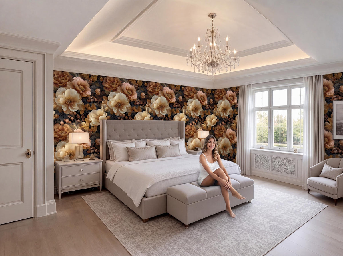 A woman sits on a bench in a luxurious bedroom with a large bed, floral wallpaper, and a chandelier overhead.