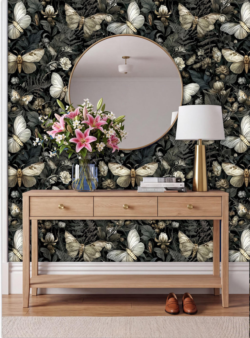 a wooden console table with a vase of pink flowers, a round mirror, and a lamp, set against a wall with a butterfly wallpaper.