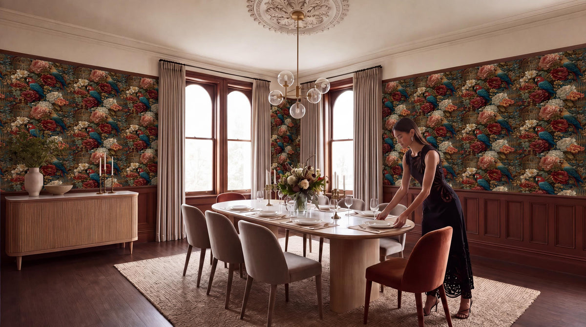 A woman in a black dress is setting the table in a dining room with a floral wallpaper, a chandelier, and a large window.