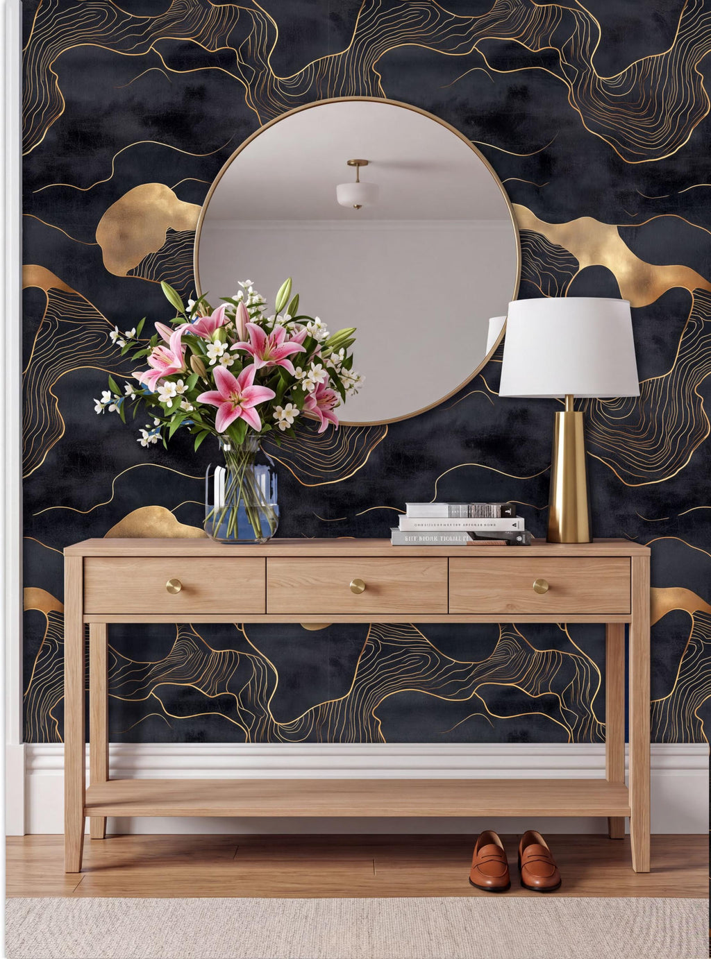 a modern interior design with a wooden console table, a round mirror, a vase of pink flowers, a lamp, and a pair of brown shoes. The wall behind the table has a black and gold abstract pattern.