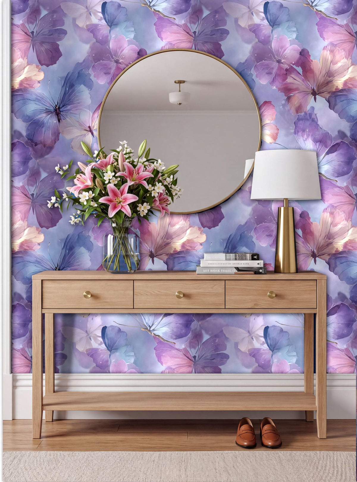 a wooden console table with a round mirror above it, set against a vibrant purple and blue floral wallpaper. The table has three drawers and a lamp on it. A vase of pink flowers is placed on the table, and a pair of brown shoes can be seen on the floor next to the table.