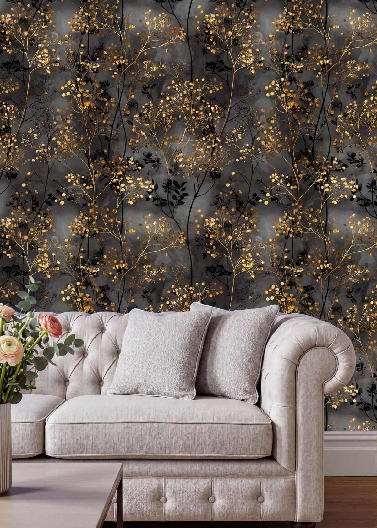 a luxurious living room with a white tufted sofa and a gray armchair, both adorned with gray and gold throw pillows. The sofa is positioned against a wall with a striking black and gold wallpaper pattern, which complements the overall decor of the room. A vase of flowers is placed on the floor next to the sofa, adding a touch of natural beauty to the space.