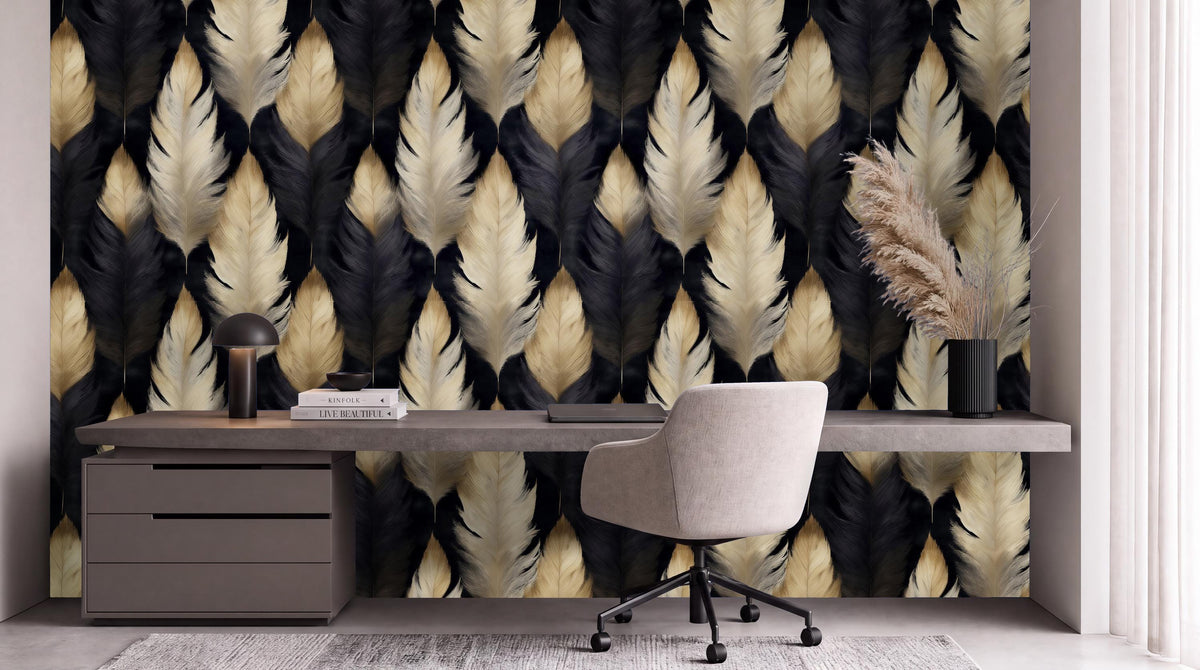 a modern workspace with a large wallpapered wall displaying a repeating pattern of black, white, and gold feathers. The workspace includes a gray desk with a chair, a lamp, and a vase with dried flowers.