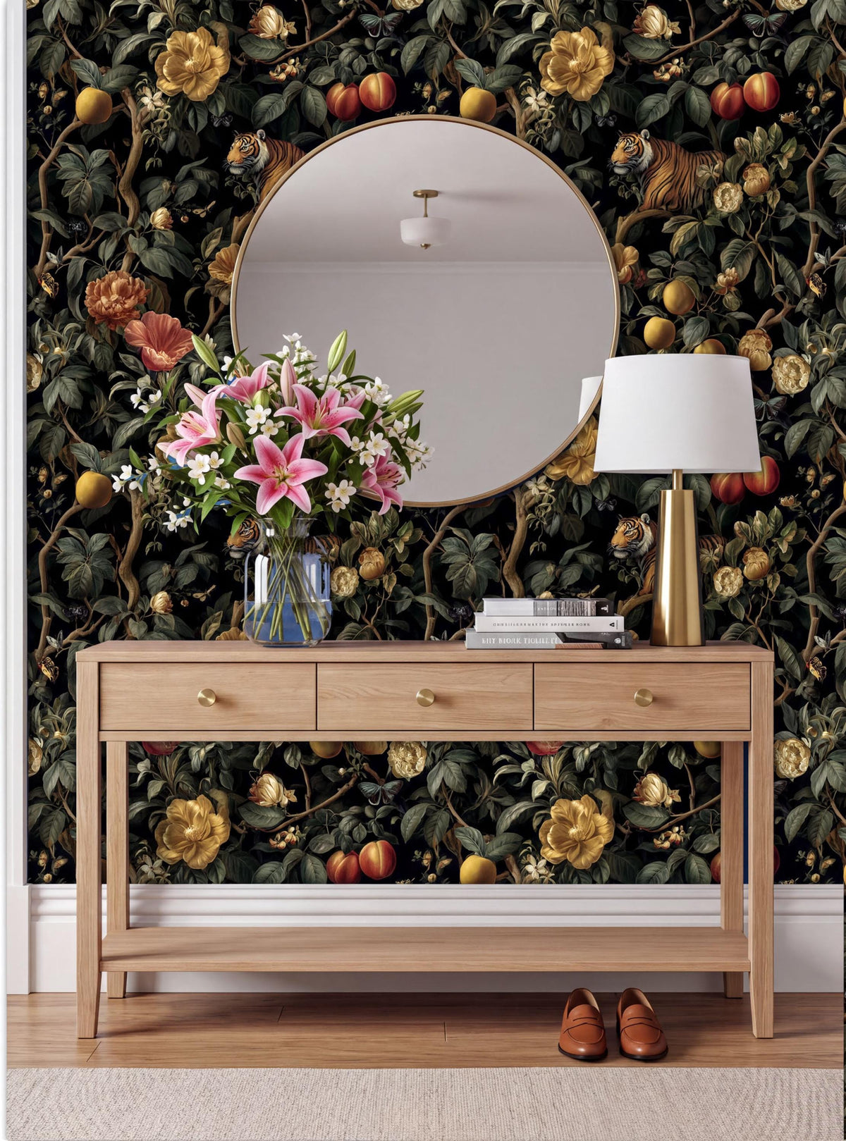 a wooden console table with a round mirror above it, set against a wall with a vibrant floral wallpaper. The table has a vase of pink flowers and a lamp, creating a cozy and inviting atmosphere.