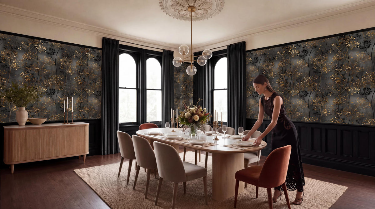 A woman in a black dress is setting the table in a dining room with a large chandelier overhead, a wooden table with chairs, and a vase of flowers on the table.
