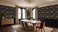 a formal dining room with a large wooden table surrounded by six chairs. The walls are adorned with a black and gold wallpaper pattern featuring bees and flowers. The room is illuminated by a chandelier and natural light coming through two large windows. The dining table is set with a vase of flowers and candles, creating a warm and inviting atmosphere.