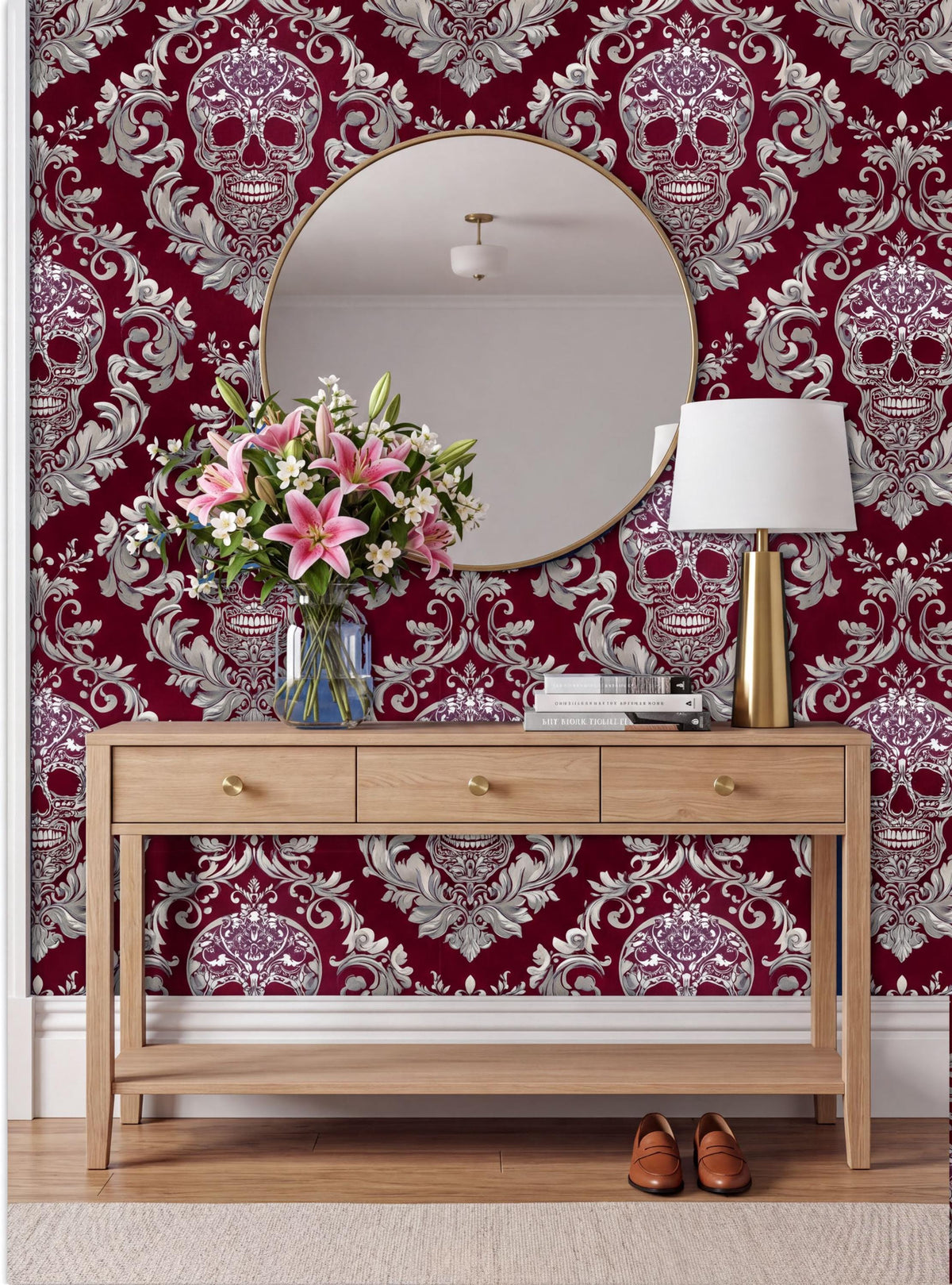 a wooden console table with a round mirror above it, set against a wall with a red and white damask pattern. The table has a vase of pink flowers and a lamp on it. The wall behind the table has a large, ornate mirror with a gold frame.