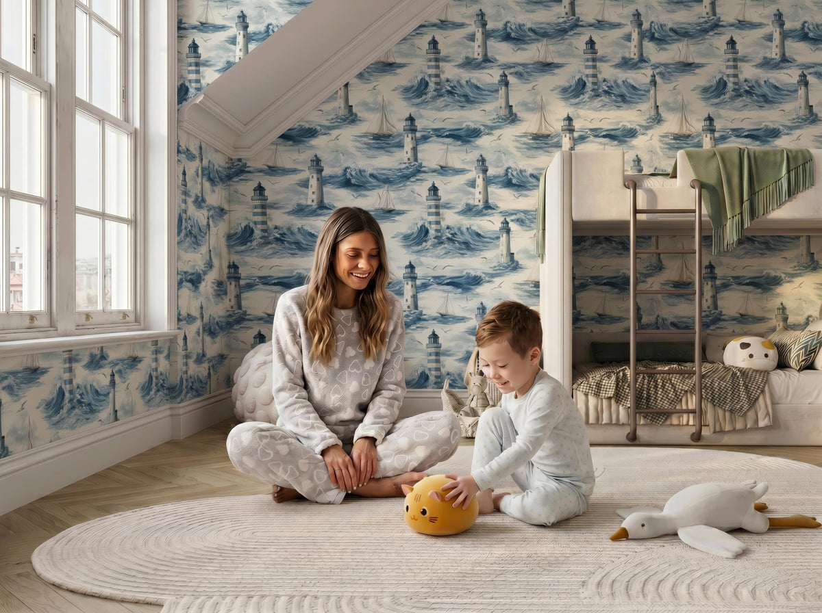A woman and a young boy are sitting on the floor in a bedroom with a blue and white lighthouse wallpaper. The woman is smiling and the boy is playing with a stuffed animal.
