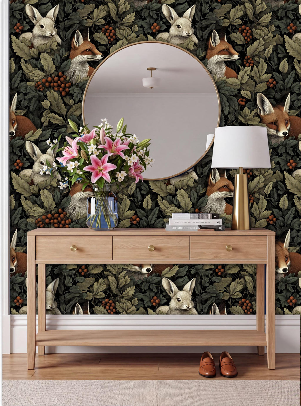 a wooden console table with a vase of pink flowers, a lamp, and a round mirror on a wall with a fox and rabbit wallpaper.