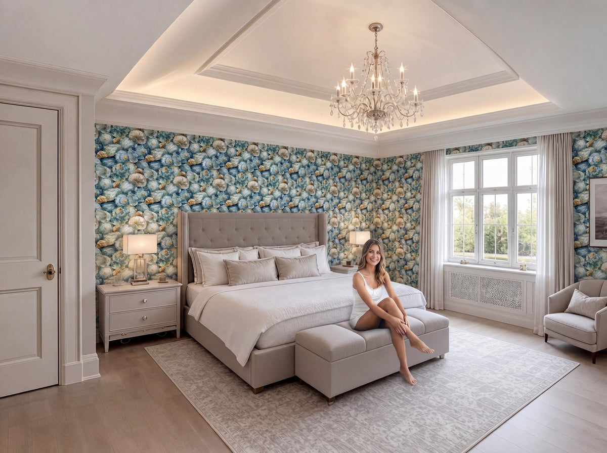 A woman sits on a bench in a luxurious bedroom with a large bed, a chandelier, and a floral wallpaper.