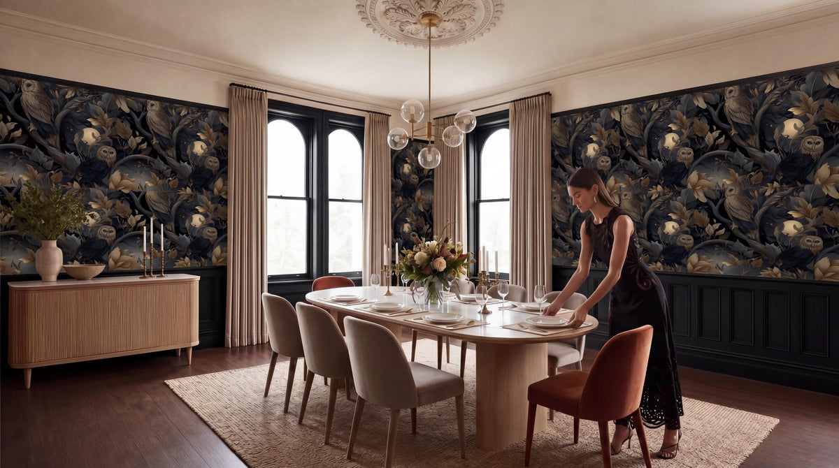 A woman in a black dress is setting the table in a dining room with a large floral wallpaper, a chandelier, and a wooden table with chairs.