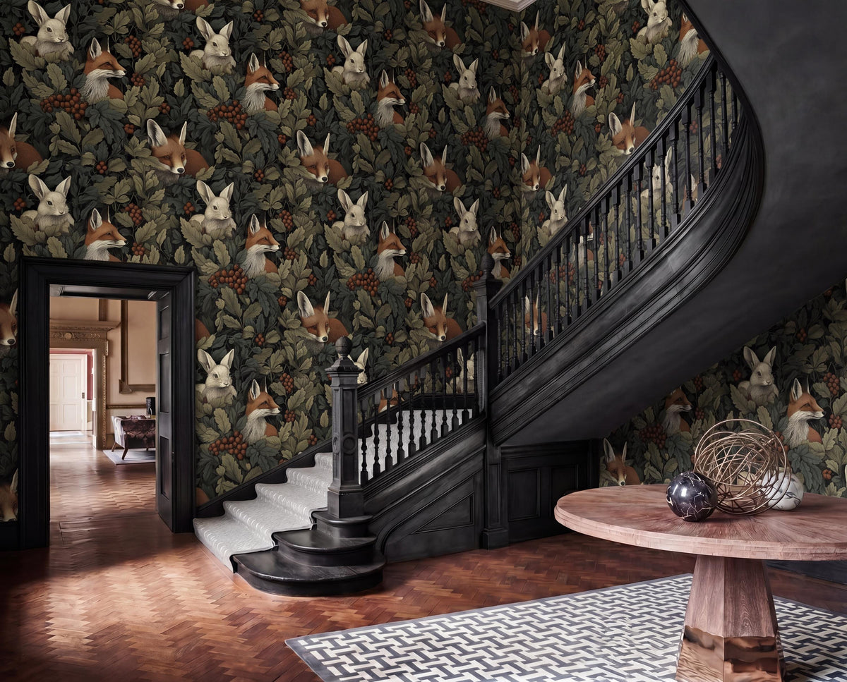 a hallway with a wooden staircase, a round wooden table, and a patterned rug on the floor. The walls are covered in a wallpaper with a repeating pattern of foxes and leaves.