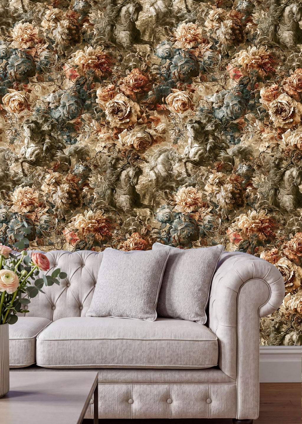 a cozy living room setting with a tufted cream-colored sofa adorned with two gray throw pillows. The sofa is positioned in front of a wall covered in a floral wallpaper, creating a warm and inviting atmosphere. A vase of flowers is placed on the floor next to the sofa, adding a touch of natural beauty to the space.