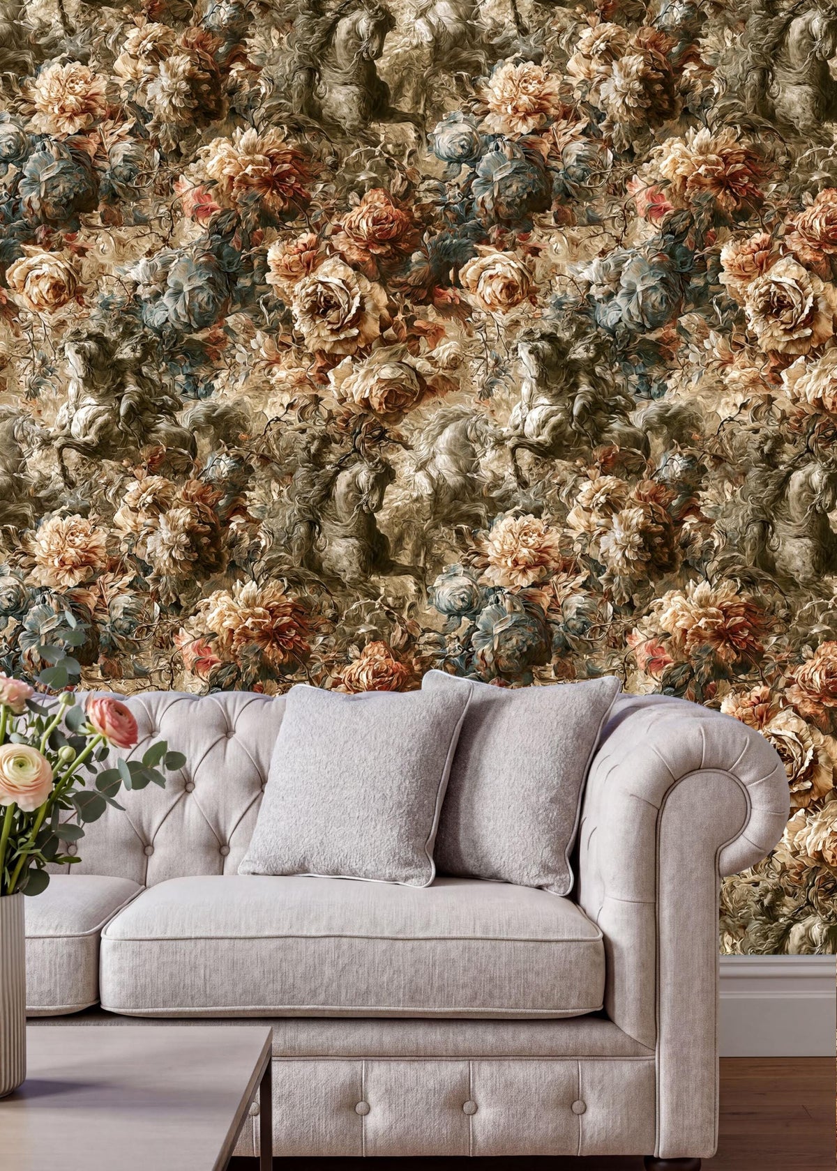 a cozy living room setting with a tufted cream-colored sofa adorned with two gray throw pillows. The sofa is positioned in front of a wall covered in a floral wallpaper, creating a warm and inviting atmosphere. A vase of flowers is placed on the floor next to the sofa, adding a touch of natural beauty to the space.
