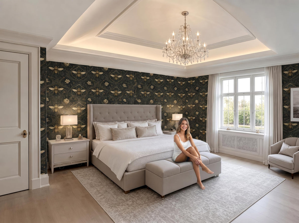 A woman sits on a bench in a luxurious bedroom with a large bed, a chandelier, and a patterned wallpaper.