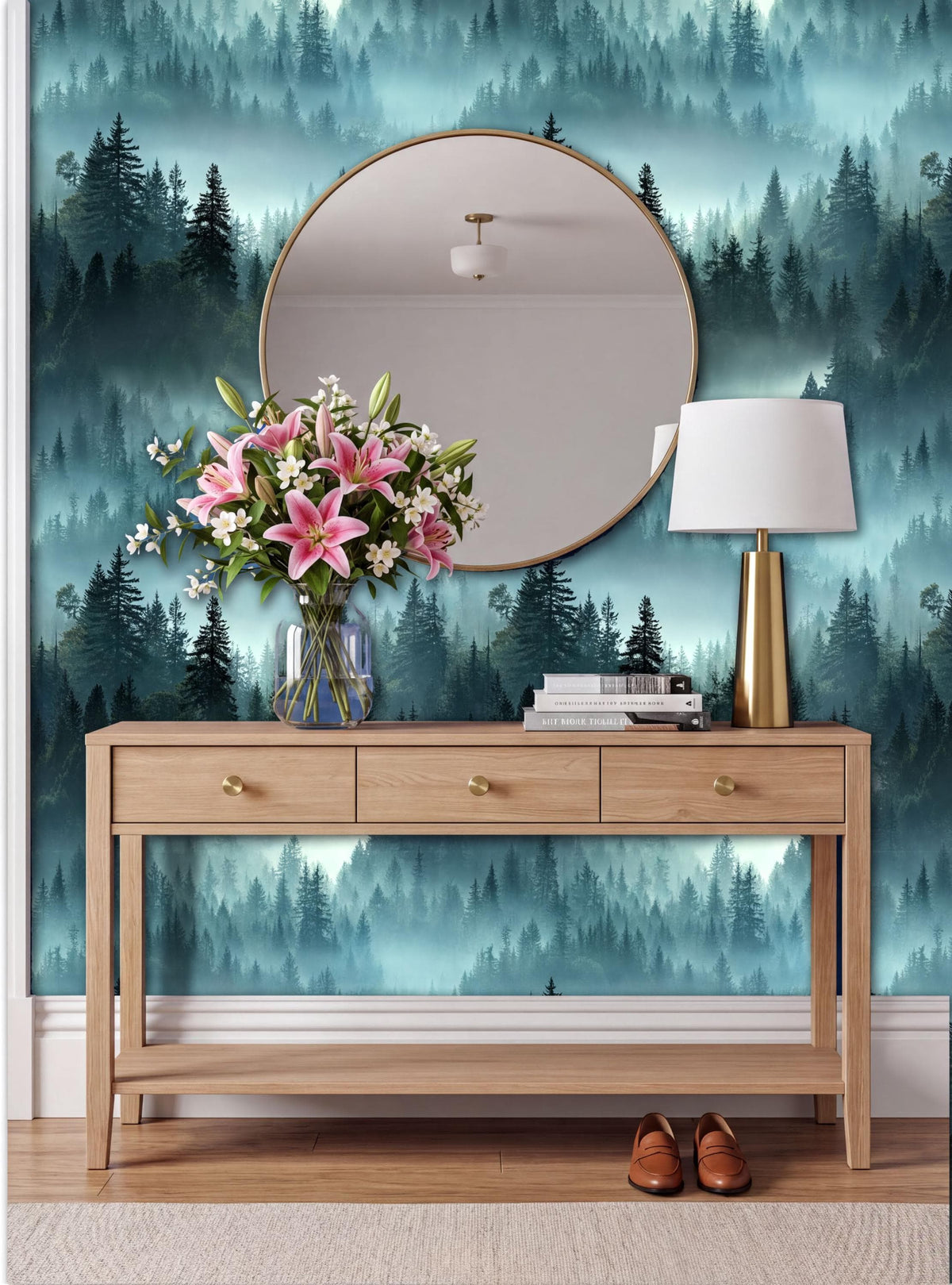 a wooden console table with a vase of pink flowers, a round mirror, and a lamp, set against a forest-themed wallpaper.