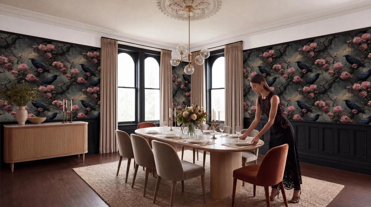A woman in a black dress is setting the table in a dining room with a floral wallpaper, a chandelier, and a large window.