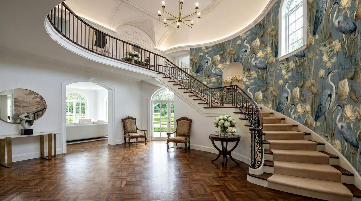a grand, luxurious entryway with a curved staircase, ornate railings, and a large chandelier overhead. The walls are adorned with a floral wallpaper, and the wooden floor adds to the elegance of the space. The room is filled with natural light from the windows, creating a warm and inviting atmosphere.