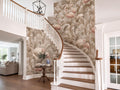 a well-decorated entryway with a spiral staircase, a wooden table with a vase of flowers, and a chandelier hanging above. The walls feature a floral wallpaper with pink flamingos, and the overall color scheme is neutral, with white and beige tones.