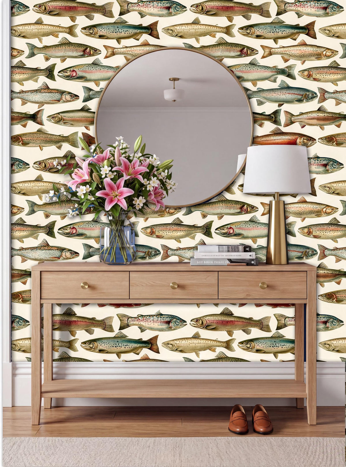 a wooden console table with a vase of pink flowers, a round mirror, and a lamp, set against a wall with a fish wallpaper.