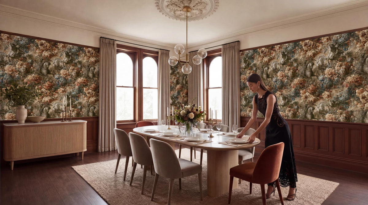 A woman in a black dress is setting the table in a dining room with floral wallpaper, a chandelier, and a large dining table with chairs.