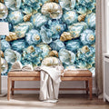 a wallpapered wall with a large, colorful pattern of seashells and flowers in shades of blue, green, and gold. In front of the wall, there is a wooden bench with an open book and a white blanket draped over it.