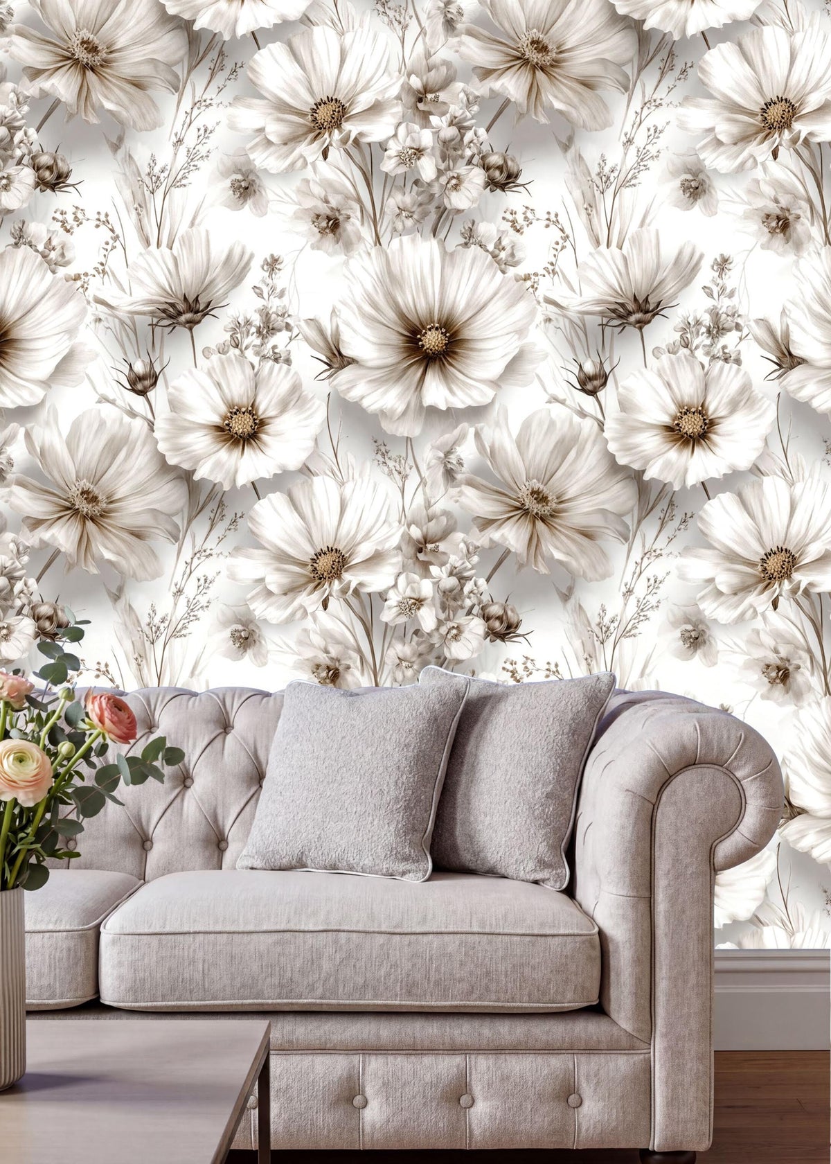 a living room with a gray tufted sofa and a vase of flowers on a coffee table. The sofa is positioned against a wall with a floral wallpaper pattern.