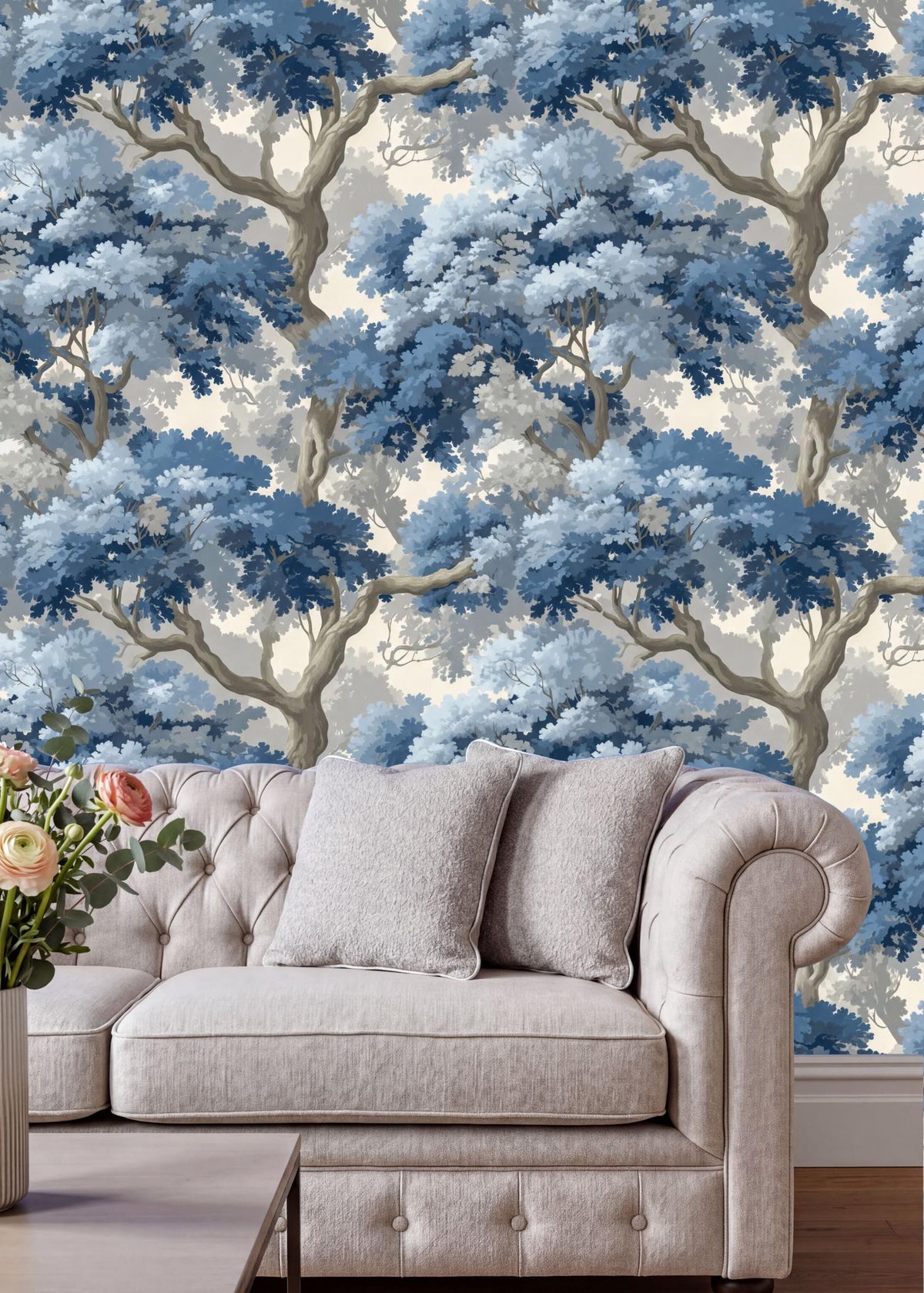 a living room with a white tufted sofa and a vase of flowers on a coffee table. The sofa is positioned against a wall with a large, intricate blue and white wallpaper depicting a forest scene.