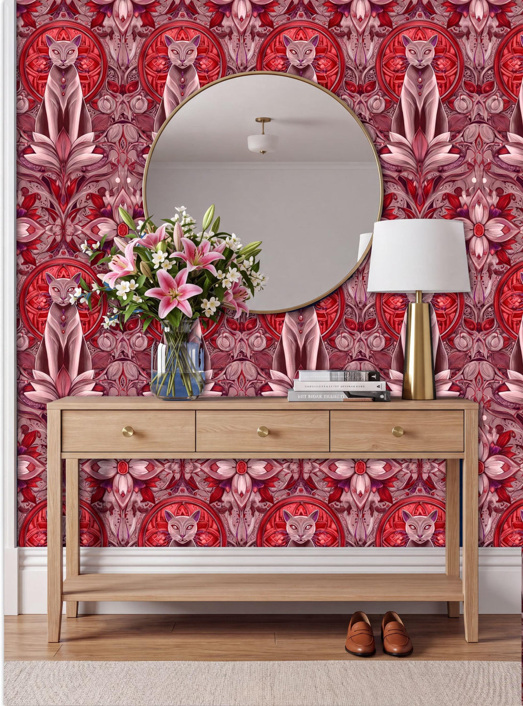 a wooden console table with a round mirror above it, set against a vibrant red and pink patterned wallpaper. The table has a vase of flowers and a lamp on it, creating a cozy and inviting atmosphere.