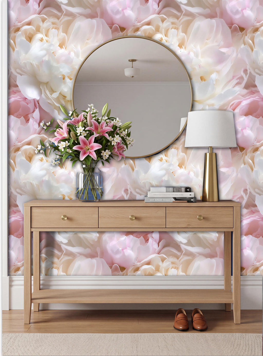 a wooden console table with a round mirror above it, a vase of pink flowers, a lamp, and a pair of brown shoes placed on the floor.