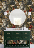 a bathroom vanity with a green cabinet and a white countertop. The vanity has a round mirror above it, and there are two wall sconces on either side of the mirror. The wall behind the vanity has a floral wallpaper pattern in shades of green, gold, and red.