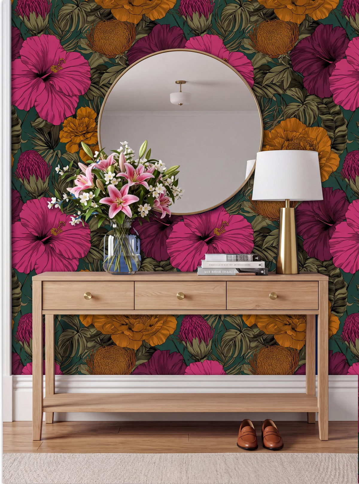 a wooden console table with a round mirror above it, set against a vibrant floral wallpaper. The table has three drawers and a vase of flowers on top. A lamp is also present on the table. The overall scene has a warm and inviting atmosphere.