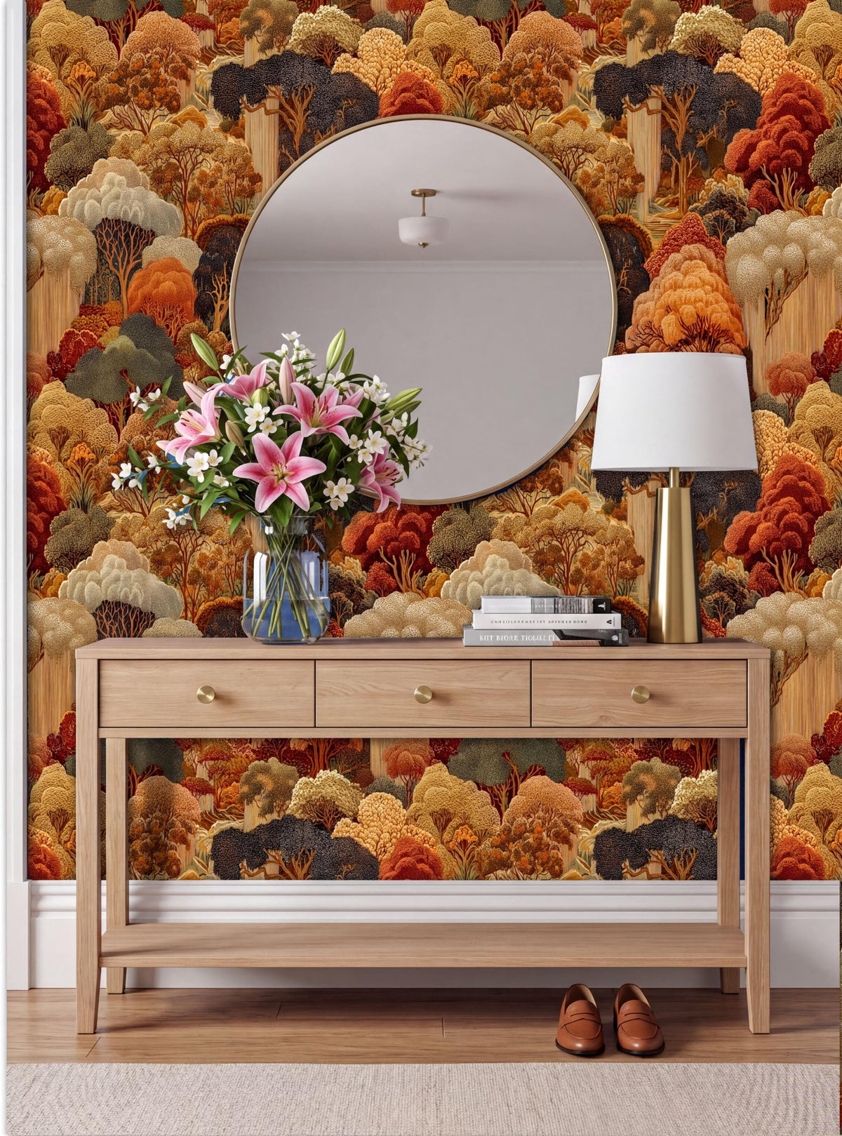 a wooden console table with a round mirror above it, set against a wall with a vibrant, colorful wallpaper depicting a forest scene. The table is adorned with a vase of pink flowers, a lamp, and a stack of books. A pair of shoes is placed on the floor next to the table.